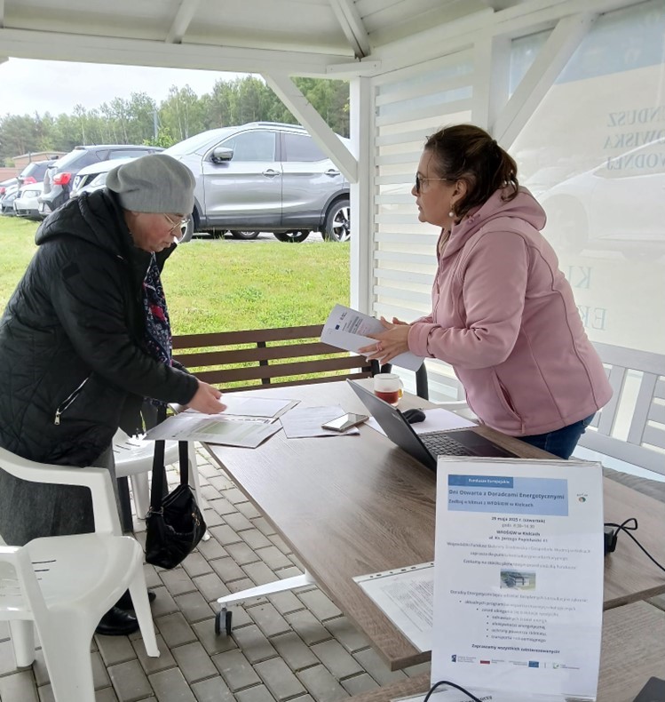 na zdjęciu doradca energetyczny pod namiotem przy stoliku rozmawia z potencjalnym beneficjentem źródeł finansowania