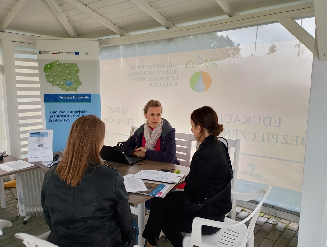 na zdjęciu doradca energetyczny pod namiotem przy stoliku rozmawia z potencjalnym beneficjentem źródeł finansowania