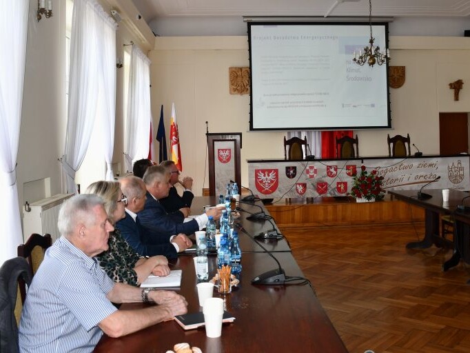 uczestnizy spotkania siedzą przy stołach i słuchają wystąpienia prelegenta