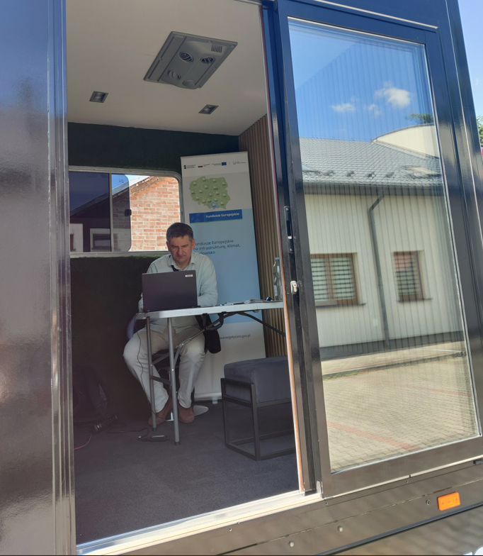 Doradca energetyczny siedzi przy stole w mobilnym punkcie informacyjnym