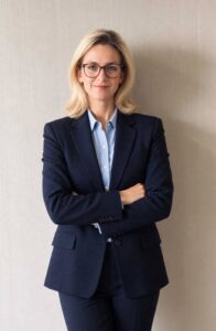 Zdjęcie kobiety, stoi wyprostowania, w garniturze granatowym, ma jasne włosy i okulary